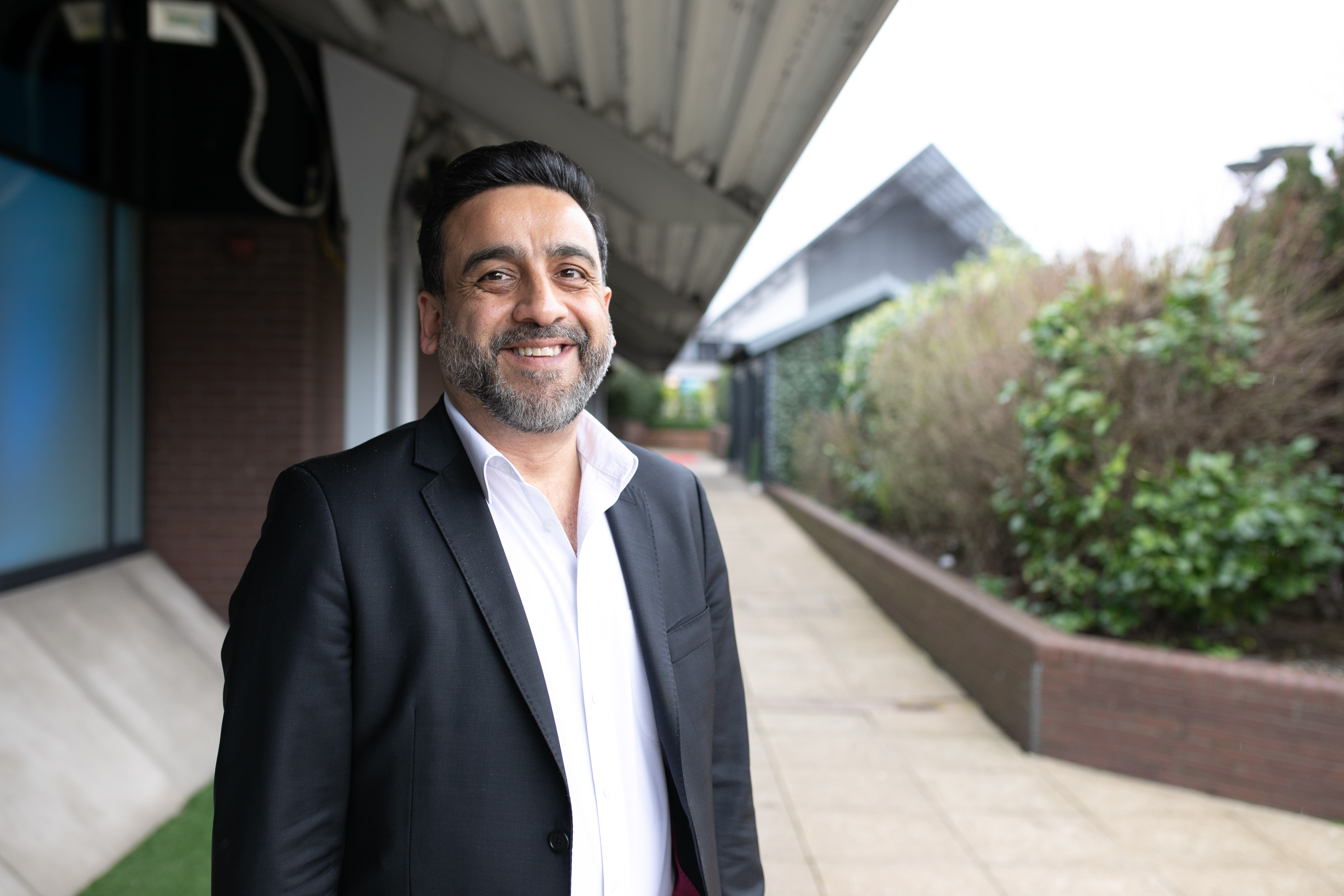 Middle aged man is standing in front of a building wearing a blazer