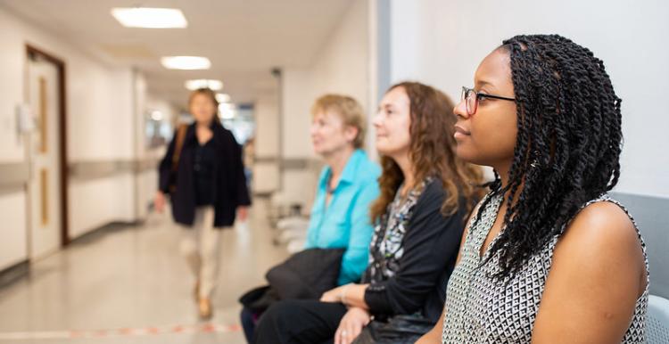 Three women sitting in the waiting room at a hospital, one woman walking by them