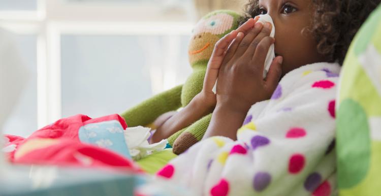 Girl resting on bed, blowing her nose with a tissue.