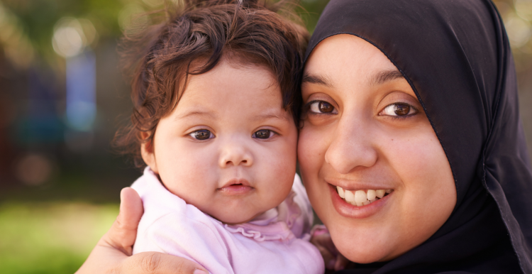 Smiling mother wearing hijab, holding her baby.