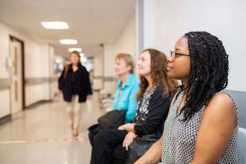 Three women sitting in the waiting room at a hospital, one woman walking by them