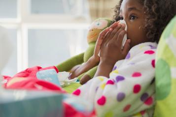 Girl resting on bed, blowing her nose with a tissue.