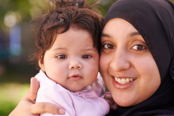 Smiling mother wearing hijab, holding her baby.